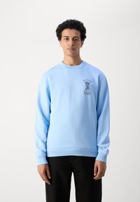 Light blue sweatshirt made of soft fabric, featuring a round neckline and long sleeves, with a black graphic logo on the chest.