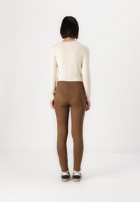 Maglione lavorato a maglia beige, leggings marroni aderenti e sneakers bianco e nere. Texture liscia, design aderente, dettagli minimi.