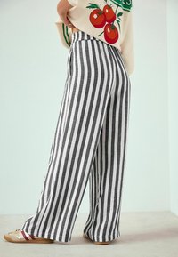 Pantaloni largi cu dungi alb-negru, cu croială lejeră, talie înaltă și material ușor, asortați cu încălțăminte casual.