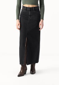 Svart denim maxi-skjørt med frontsplitt, høy midje og fem lommer. Brukt med brune hæler.