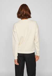 Crème-kleurige sweatshirt met een ronde halslijn, verlaagde schoudernaad en ribgebreide manchetten. Gecombineerd met zwarte broeken, die een relaxte pasvorm laten zien.