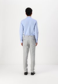 Chemise bleu clair à boutons, pantalon gris ajusté avec un motif léger en tartan, et chaussures noires, vues de dos sur un fond blanc.