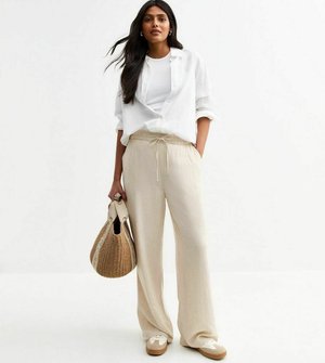 Pantalons larges beiges légers avec une taille élastique, associés à un t-shirt blanc et une chemise blanche surdimensionnée, tenant un sac tissé.