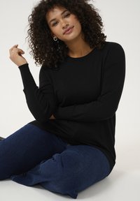 Zwarte lange mouw top met een ronde hals en ribgebreide manchetten, casual gedragen met donkerblauwe jeans terwijl zittend.