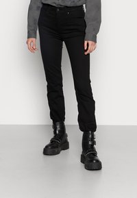 Black jeans with a slim fit, made of denim. Paired with chunky black boots featuring buckles. Grey button-up shirt with a textured pattern.