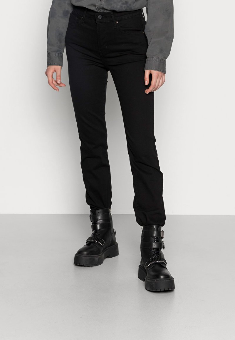 Black jeans with a slim fit, made of denim. Paired with chunky black boots featuring buckles. Grey button-up shirt with a textured pattern.
