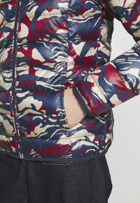 Gewatteerd jack in marineblauw met een rood-beige camouflerend patroon. Voorzien van een ritssluiting aan de voorkant en steekzakken aan de zijkant. Gladde, glanzende stof.
