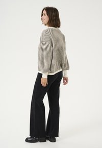 Pulover tricotat gros în crem și negru, cu un croi lejer, umeri lăsați și manșete cu nervuri. Asortat cu pantaloni negri cu talie înaltă.