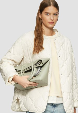 Gep quiltete cremefarbene Jacke mit silbernen Druckknöpfen, kombiniert mit einer hellgrünen Lederhandtasche im eckigen Design und mit Reißverschlussfächern.