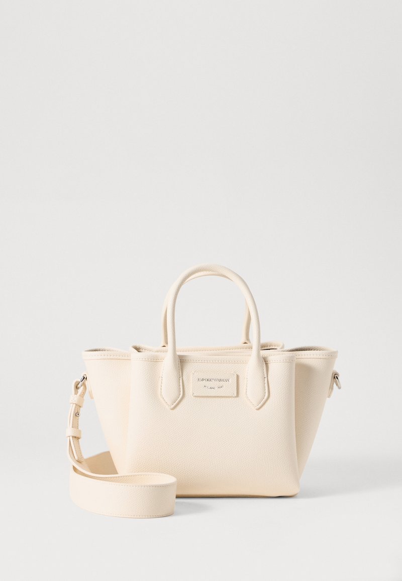 Bolso de mano de cuero beige con acabado texturizado, asas cortas y correa ajustable. Presenta una placa rectangular con el logo en la parte frontal.
