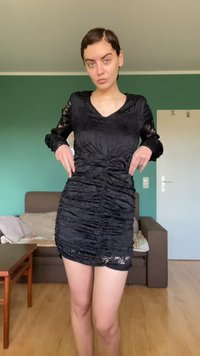 Juoda suknelė su raukšlėtu audiniu, ilgi nėriniai rankovės, V formos iškirpte, aptempianti figūra ir kraštas virš vidurinės šlaunies dalies.