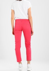 Růžové úzké kalhoty z bavlněné směsi, s pasem ve střední výšce, zadními kapsami a zúženými nohavicemi, kombinované s bílými teniskami.