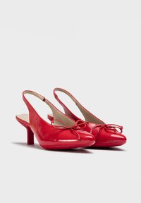 Escarpins slingback vernis rouges avec un bout pointu, un petit nœud en accent et un talon bloc modéré. Texture lisse et design épuré.
