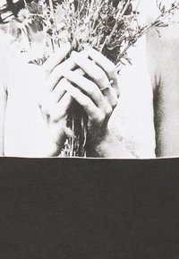 Camiseta gráfica en blanco y negro que presenta manos sosteniendo tallos de flores, con una sección inferior negra texturizada, creando un diseño contrastante.
