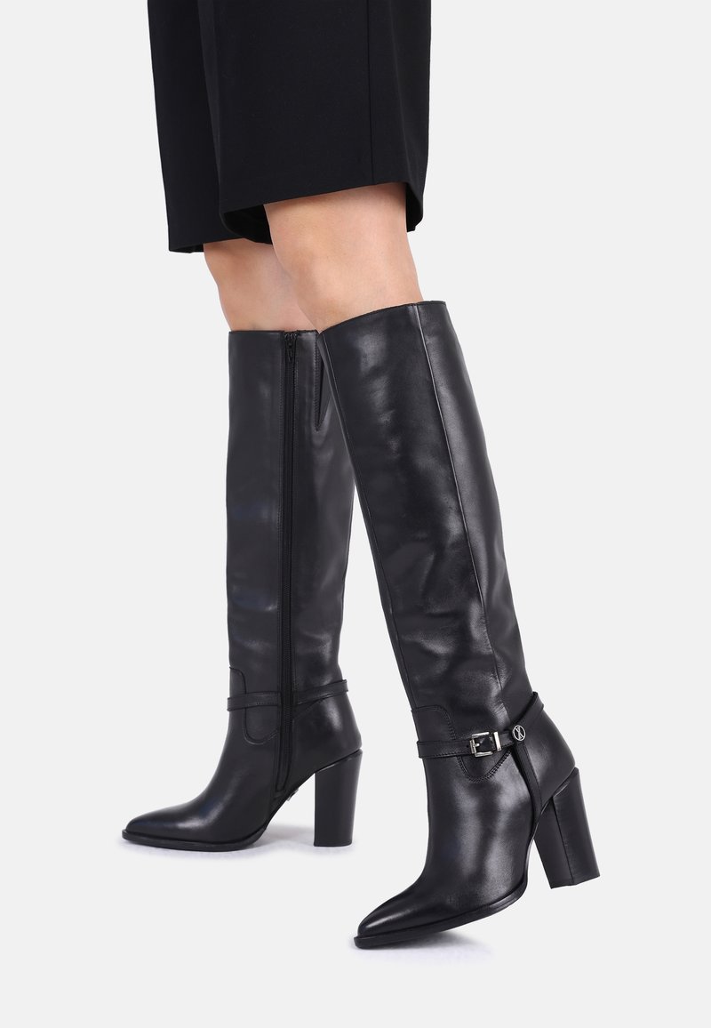 Schwarze Stiefel aus Leder bis zum Knie mit spitzem Schuhkopf, Blockabsatz, seitlichem Reißverschluss und verstellbarem Knöchelriemen. Glatte Textur, elegantes Design.