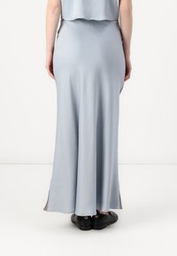 Jupe longue, bleu pastel, en tissu lisse, avec une forme évasée et des fentes latérales, accompagnée de chaussures noires.