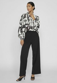 Blusa con estampado en blanco y negro, con mangas abullonadas, combinada con pantalones de pierna ancha negros y tacones negros destalonados. Tela suave y corte ajustado.