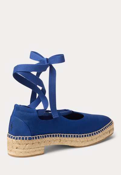 Plava espadrila od tkanine s trakama za vezanje oko gležnja i ispletenim đonom od jute, prikazana s boka na svijetloj pozadini.