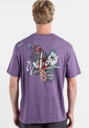 T-shirt violet à manches courtes avec motifs floraux et texte au dos. Le design comprend des accents blancs et des éléments à motif damier.