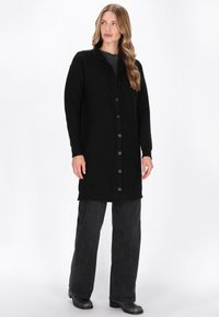 Czarny, dziany kardigan w zygzakowy wzór, z kołnierzykiem i zapięciem na guziki. W zestawie z ciemnymi spodniami typu wide-leg i botkami.