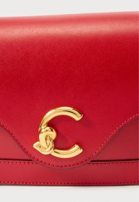 Borsa a mano in pelle rossa con design ondulato, accessori in tonalità oro e chiusura con logo distintivo. Texture liscia con dettagli di cuciture.