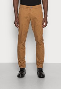 Chinos de algodón marrón con un ajuste ajustado, bolsillos frontales y un cierre de botón. Combinados con zapatos negros de cordones para un look completo.