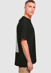 Sort bomulds T-shirt med løs pasform, prydet med et stort puslespil-design i grå på bagsiden og et lille logo på forsiden.