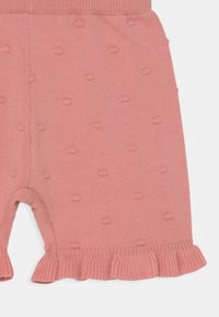 Os calções tricotados cor-de-rosa apresentam um padrão texturizado de bolinhas, uma cintura canelada e uma bainha franzida. O material é macio e leve.
