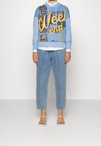 Niebieska bluza z kapturem z grafiką "Weel end", w połączeniu z jasnoniebieskimi, wysokimi dżinsami i przezroczystymi sandałami. Gładki materiał, luźny krój.