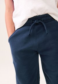 Tumesinised dressipüksid, millel on nööriga vöökoht, küljetaskud ja pehme, tekstuuriga kangas. Põlveni lõppevad ja mugava lõikega.