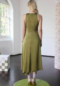 Alyvuogių žalios satino suknelė su prigludusia liemene, plakta apatine dalimi ir gėlių apvadu ant iškirptės, derinama su geltonais aukštakulniais sandalais.