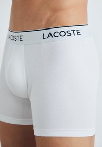 Fehér pamut boxer alsónadrág, fekete-fehér "LACOSTE" logós derékkal, szoros illeszkedéssel és sima textúrával.