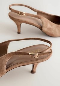 Zapatos de tacón slingback en ante color tostado con una correa delgada y hebilla dorada. Presentan una punta afilada y un tacón de stilettos de 7 cm para un perfil elegante.