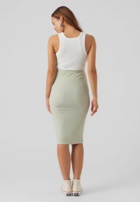 Top de alças branco canelado e saia midi justa verde pálido, com uma textura suave e um leve elasticidade. Combinado com ténis de tonalidade clara.