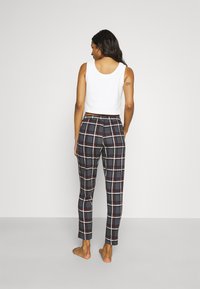 White sleeveless top paired with fitted plaid pants in navy, red, and white, featuring an elastic waist and straight legs.