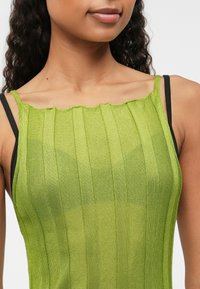 Zielony, żebrowany top na ramiączkach z falbaniastym dekoltem, z cienkimi czarnymi paskami. Materiał wydaje się lekki i gładki w dotyku.