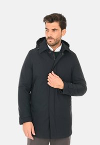 Parka nera con cappuccio, dotata di zip frontale e bottoni, tasche laterali e una texture liscia. Design casual, lunghezza media.