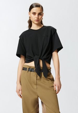 T-shirt nera croppata a maniche corte, con dettaglio nodo frontale e logo ricamato. Abbinata a pantaloni khaki a vita alta e una cintura nera con accenti.