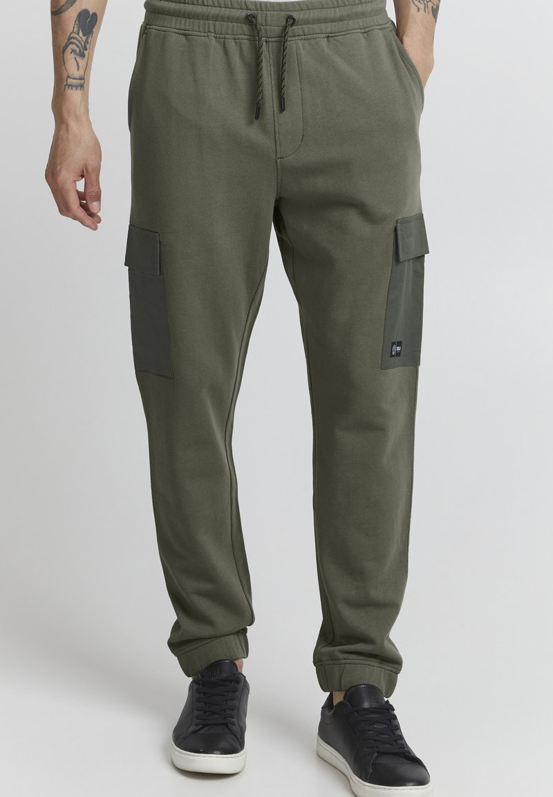 Olive green joggers with a relaxed fit, elastic waistband, and side cargo pockets featuring a dark panel. Fabric is soft with a smooth texture.