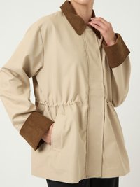 Μπεζ μπουφάν με καφέ βελόνα στο γιακά και τα μανίκια, με σφιγμένη μέση, πλαϊνές τσέπες, φορεμένο από άτομο που ρυθμίζει το γιακά.