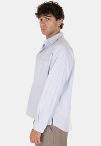 Camicia a maniche lunghe a righe blu chiaro, con chiusura a bottoni, taschino sul petto, taglio dritto, con polsini a bottoni e spacco laterale.