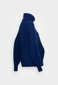 Marinblå oversized turtleneck-tröja med ribbad textur, som har sänkta axlar och långa ärmar, vilket ger en avslappnad passform.