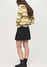 Maglione a righe in giallo, rosa e marrone con vestibilità ampia, abbinato a una gonna nera a trapezio e a stivali neri con lacci.