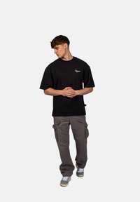 Černé bavlněné tričko s bílým vyšívaným logem, spárované se šedými cargo kalhotami s bočními kapsami a volným střihem. Součástí jsou i pohodlné boty.