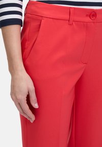 Czerwone dopasowane spodnie uszyte z gładkiego, lekkiego materiału. Posiadają boczne kieszenie oraz zapięcie na guzik w pasie.