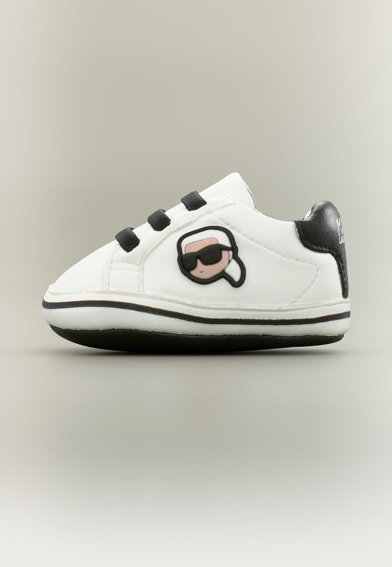 Fehér és fekete baba tornacipő fekete fűzőkkel, oldalán napszemüveget viselő rajzfilmfigurával és fekete sarokpánttal.