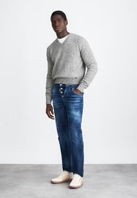 Gray knitted sweater, blue denim jeans with a slight fade, and white sneakers with tan accents. Standing pose against a neutral background.