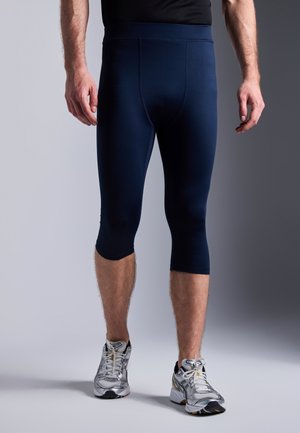 Leggings athlétiques bleu marine, arrivant au genou, avec une texture lisse, dotés d'une large ceinture et de coutures plates, associés à des chaussures de course argentées.