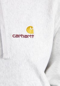 Gray sweatshirt with a zipped collar. Features embroidered yellow and burgundy Carhartt logo on the chest. Soft texture and casual design.