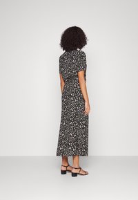 Bloemrijke maxi-jurk van zwarte stof met korte mouwen. Heeft een groen en roze bloemenpatroon en een cinched taille. Gecombineerd met zwarte hoge sandalen.